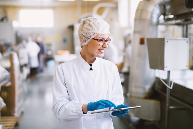 Une femme dans une usine porte des lunettes, des gants bleus et un filet à cheveux